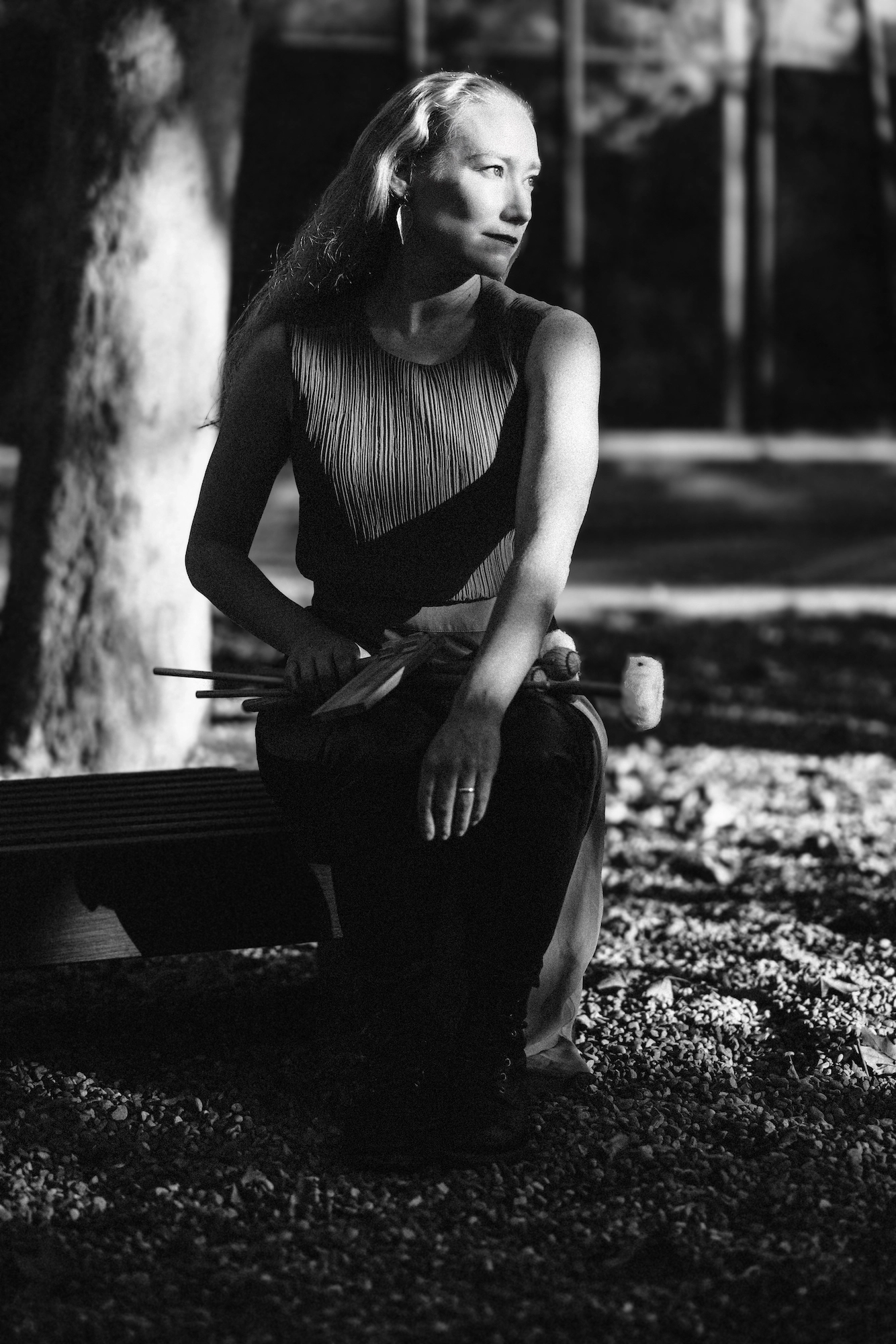 a black and white photo of Bonnie Whiting, sitting on a bench in a park with mallets in her hand