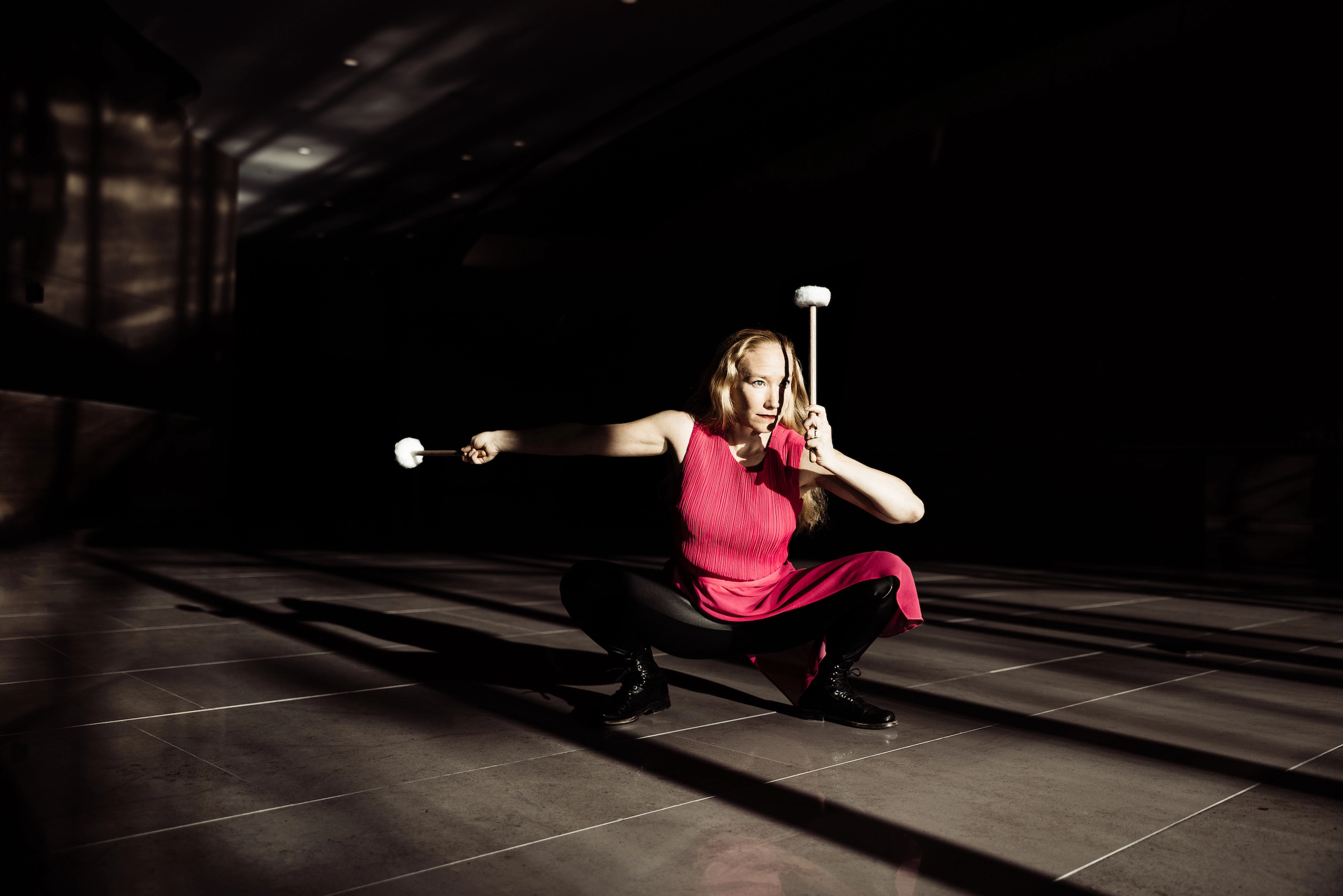 a photo of Bonnie Whiting in performance, in a low squat holding two large mallets